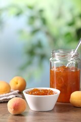 Tasty apricot jam and fresh fruits on wooden table against blurred background, closeup