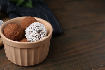 Delicious homemade candies with cocoa powder and coconut flakes in bowl on wooden table, closeup. Space for text
