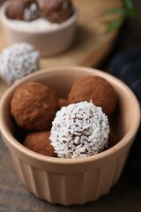 Delicious homemade candies with cocoa powder and coconut flakes in bowl on wooden table, closeup