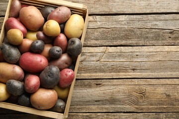 Different types of potatoes in crate on wooden table, top view. Space for text