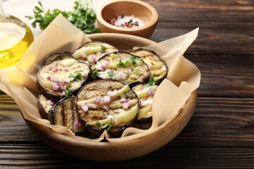 Grilled slices of eggplant with sauce, parsley and onion served on wooden table, closeup
