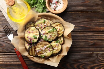 Grilled slices of eggplant with sauce, parsley and onion served on wooden table, flat lay