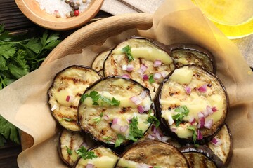 Grilled slices of eggplant with sauce, parsley and onion served on wooden table, closeup