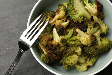 Tasty fried broccoli and fork on black table, top view
