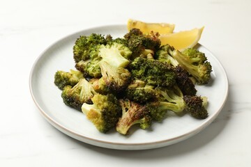 Tasty fried broccoli and lemon on white marble table, closeup