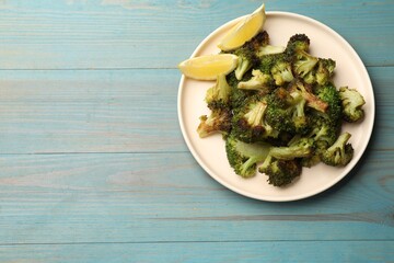 Tasty fried broccoli and lemon on light blue wooden table, top view. Space for text