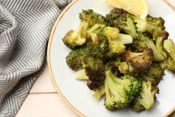 Tasty fried broccoli and lemon on light wooden table, top view