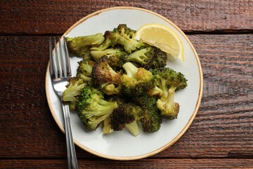 Tasty fried broccoli, fork and lemon on wooden table, top view