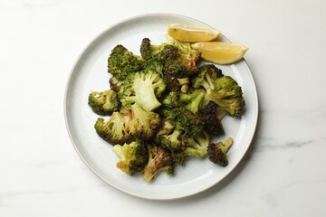 Tasty fried broccoli and lemon on white marble table, top view
