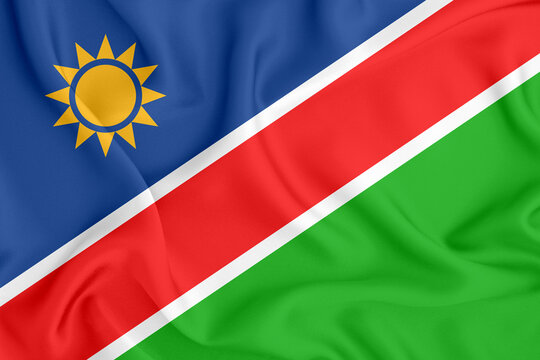 flag of the Republic of Namibia with a diagonal stripe and a yellow sun on satin fabric with folds and shadows