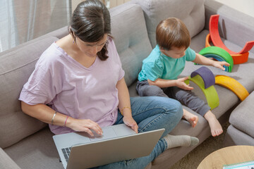 Remote working mother beside toddler engaged in independent play