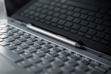 A grey stylus pen in the middle of laptop keyboard and screen