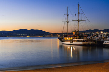 Gelendzhik resort beach. A large ship is docked at a pier, with the sun setting in the background