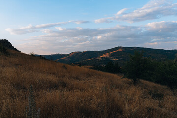 A beautiful landscape with a mountain range in the background. The sky is clear and the sun is setting, creating a warm and peaceful atmosphere