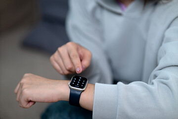 Asian young adult person finger touching smartwatch screen inputting pin code secure smart wearable technology device access control indoors home.