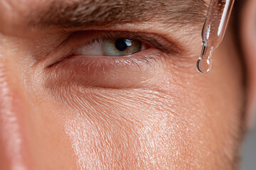 Close up of male eye with smooth glowing skin and dropper applying serum, highlighting skincare and facial treatment for healthy appearance and hydration