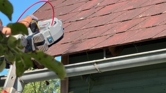 specialist inspecting clogged roof gutter with drill and camera