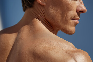 Naklejka premium Close up of man back and shoulder skin showing natural texture and wrinkles under sunlight with blurred blue background, highlighting healthy and smooth skin surface