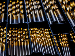 A metal drill bit with golden brass-colored hard coating rests in a drill box. The shiny surface...