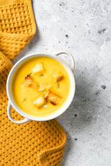 Pumpkin soup with croutons and seeds in a white handled bowl on mustard cloth. Top view, flat lay.