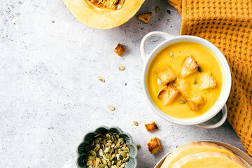 Creamy pumpkin soup in a white bowl with croutons and seeds, surrounded by fresh pumpkin, flatbread, and mustard cloth