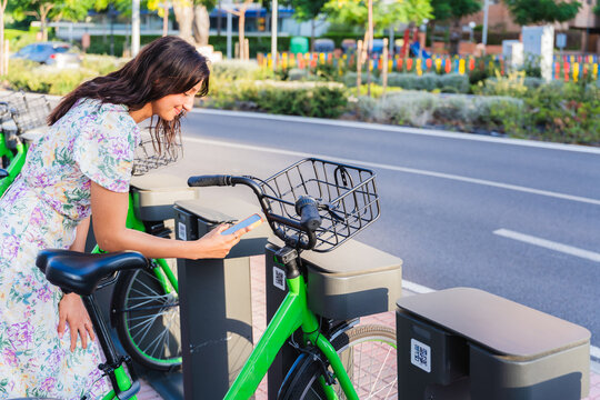 Young woman using her smartphone to unlock a shared bike in the city