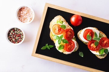Fresh homemade caprese sandwich with avocado paste, mozzarella cheese, cherry tomatoes, fresh aromatic basil leaves and spicy hot oil top view. Healthy homemade food concept.