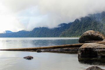 Tranquil Lake Landscape with Misty Forest Mountains and Rocks in the Foreground