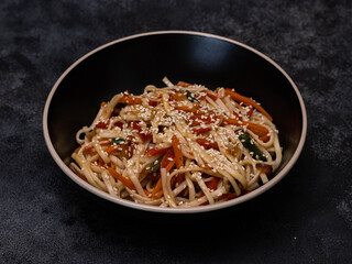 Enjoy a tantalizing bowl of stirfried noodles with colorful chilly pepper, expertly topped with fresh vibrant vegetables and sesame seeds.