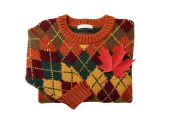 A vibrant, autumnal, multicolored knitted sweater, featuring a classic argyle pattern, and accented with a red maple leaf, lies flat against a dark background.