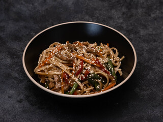 A black bowl of stirfried noodles, fresh vegetables,chicken meat and sesame, ideal for any meal or occasion on black background.