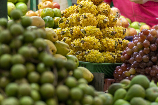 Pile of yellow pitahayas displayed at a fruit market, surrounded by mamoncillos, grapes, mangoes, and limes.
