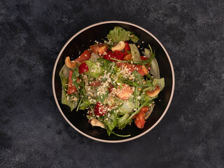 A vibrant and colorful salad mix that includes fresh greens, ripe tomatoes, crunchy cashews, and sesame seeds in black bowl on blackboard.