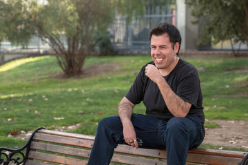 young man smiling and sitting on bench in park
