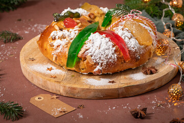 Colorful candied fruits and powdered sugar on a traditional Bolo Rei or Kings Cake, set on a wooden board amidst warm holiday decorations and lights. Is tradicional for Christmas in Portugal