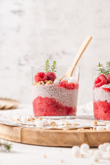 A single glass of layered raspberry and chia seed pudding topped with fresh raspberries and white crowberry on a rustic wooden platter