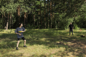 Fototapeta premium Family spending quality time together playing frisbee in open field with scenic forest view, concept of nature activities, exercise, and emotional connection between generations.