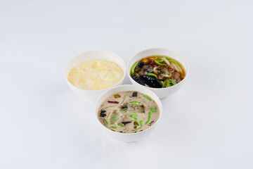 Three bowls of Asian desserts on white background. Yellow dessert, dark dessert with jelly, and a creamy dessert with green jelly pieces.