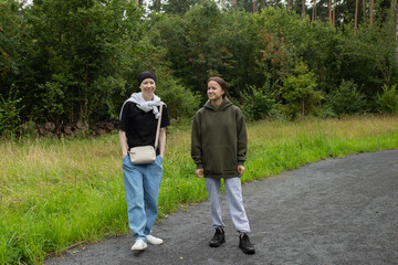 Obraz premium Outdoor friendship, two women walking along park trail in casual clothes, concept of wellness, communication and leisure activities