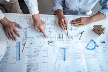 Architects or engineering team consulting and analyzing working on objects tools and construction drawings inspection planning new architectural project on blueprint and model house in modern office