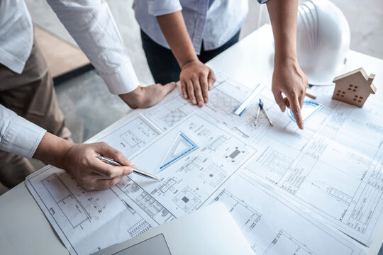 Team of architects or engineering consulting and analyzing working on objects tools and construction drawings inspection, discussing planning new architectural project on blueprint and model house