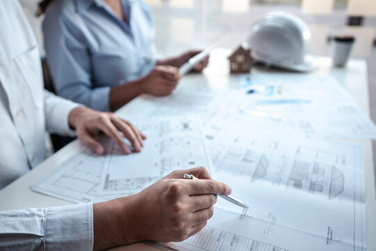 Architects or engineering team consulting and analyzing working on objects tools and construction drawings inspection planning new architectural project on blueprint and model house in modern office