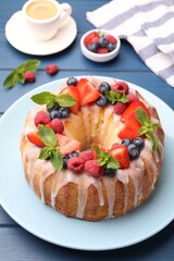 Delicious bundt cake with berries, glaze and mint on blue wooden table, closeup
