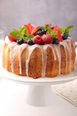 Delicious bundt cake with berries, glaze and mint on white wooden table against grey background, closeup
