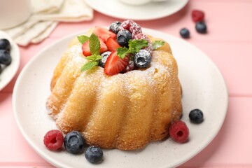Delicious bundt cake with powdered sugar, berries and mint on pink wooden table, closeup