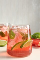 Tasty cocktail with ice cubes, lime and grapefruit on white table, closeup