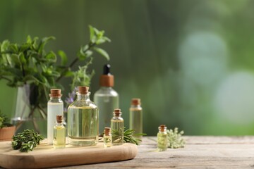 Bottles of essential oils and different herbs on wooden table outdoors, closeup. Space for text