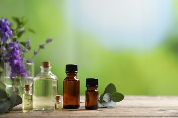 Bottles of essential oils and different plants on wooden table outdoors, closeup. Space for text