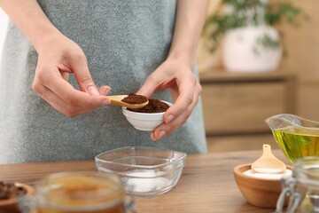 Making natural scrub. Woman adding coffee into bowl at wooden table, closeup