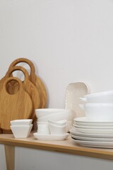 Clean dishware on wooden table near white wall